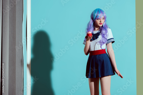stylish girl in bright wig holding cupcake and looking away in studio