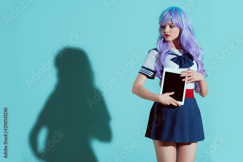 stylish girl in bright wig holding digital tablet with blank screen and looking away on blue