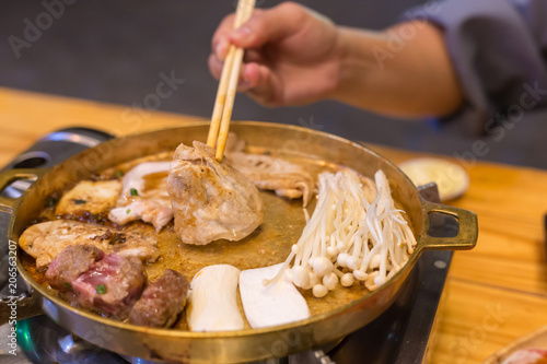 Hand holding raw pork using chopsticks on hot pan.