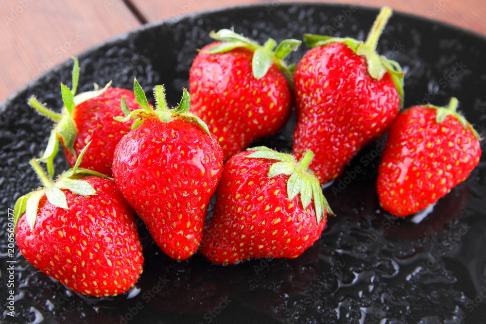 Strawberries on a black plate top view, red berries on a wooden background, fresh strawberries on dark wooden boards, vegetarian food, copy space Strawberries on a black plate top view, red berries on a wooden background, fresh strawberries on dark wooden boards, vegetarian food, copy space