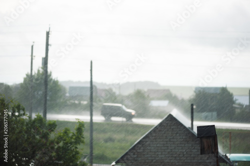 Defocused rainy image from country house, tree, pillars and car on highway. Focusing on rain. Rainy weather outside city.