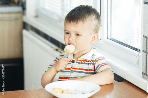 the child in the kitchen with a fork eating young potatoes
