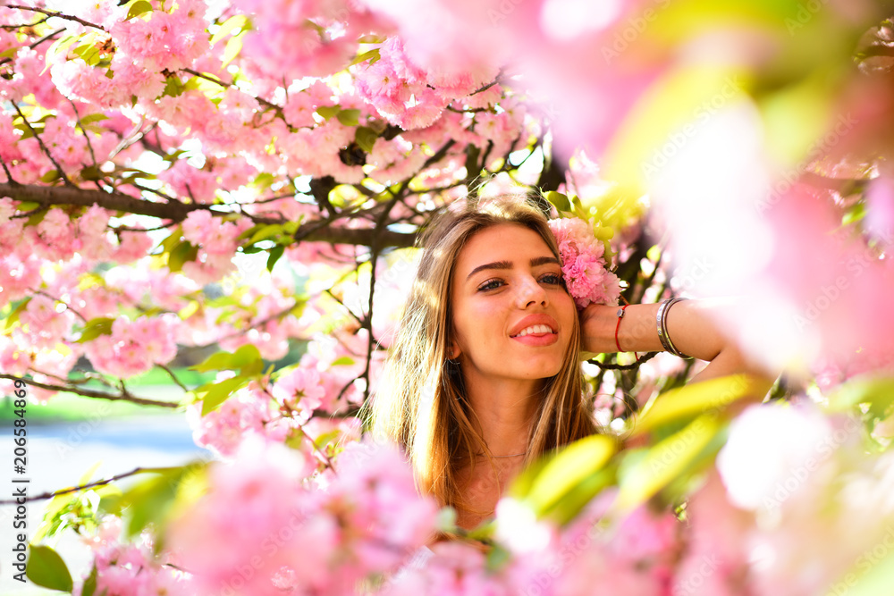 Lovely blond girl holding branch of cherry blossom. Pretty young woman posing on natural background next to blooming flowers with pink petals, spring concept Lovely blond girl holding branch of cherry blossom. Pretty young woman posing on natural background next to blooming flowers with pink petals, spring concept