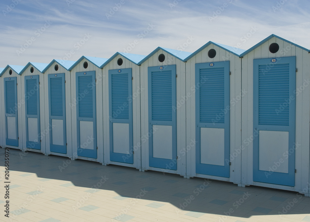 Naklejka premium wooden beach cabins by the sea, changing rooms, blue and white, used to change and put on bathing suit, vacation, summer, sun, ligurian riviera, Albenga beach, Italy