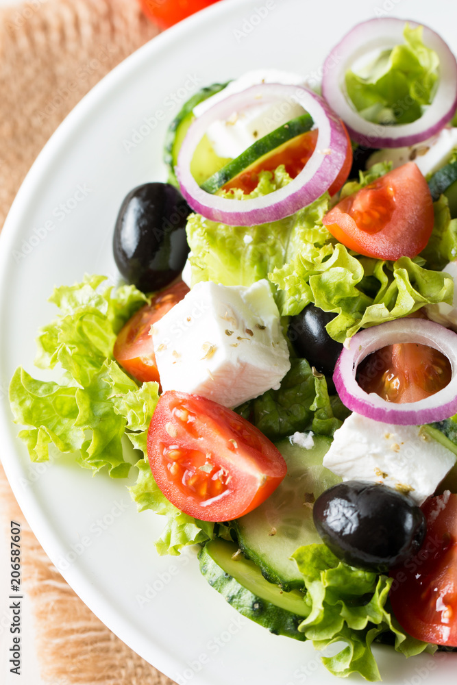 Fresh Greek salad made of cherry tomato, ruccola, arugula, feta, olives, cucumbers, onion and spices. Caesar salad in a white bowl on wooden background. Healthy organic diet food concept. Fresh Greek salad made of cherry tomato, ruccola, arugula, feta, olives, cucumbers, onion and spices. Caesar salad in a white bowl on wooden background. Healthy organic diet food concept.