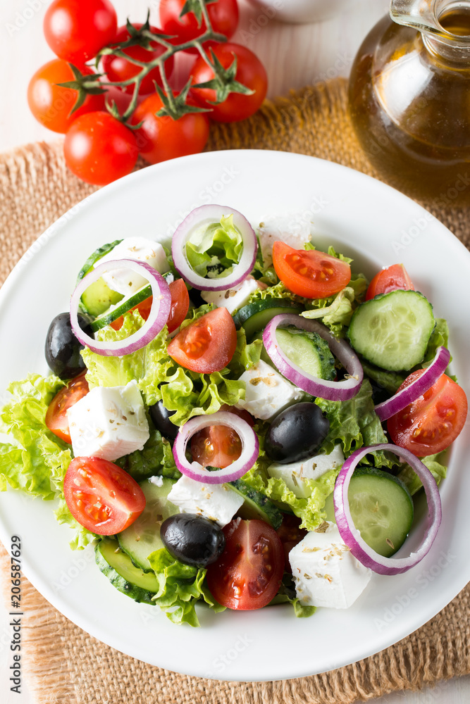 Fresh Greek salad made of cherry tomato, ruccola, arugula, feta, olives, cucumbers, onion and spices. Caesar salad in a white bowl on wooden background. Healthy organic diet food concept. Fresh Greek salad made of cherry tomato, ruccola, arugula, feta, olives, cucumbers, onion and spices. Caesar salad in a white bowl on wooden background. Healthy organic diet food concept.