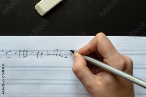 Close-up view of the female's hand writing music notes in the music sheets laying on the black background. Concept of the education in arts, music, creativity, music notes writing.