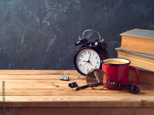 Coffee cup, alarm clock and old books on vintage wooden table