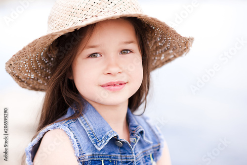 Smiling chiild girl 4-5 year old wearing funny straw hat closeup. Summer time. Childhood.