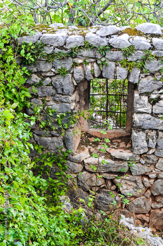 An ancient stone wall of a ruined house with a door among the grass. Old house, ruins, background