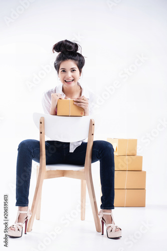The lady in white shirt and blue jean is posing by sitting on wooden chair and hold shopping post box in hand,