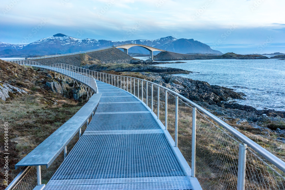 View of the Storseisundet Bridge with mountains in the background from the elevated path at Eldhusøya on the Atlantic Road in Norway