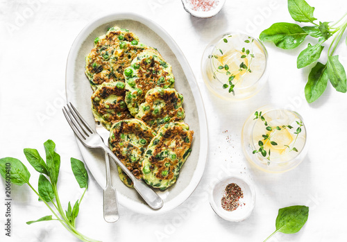 Cuadro en lienzo Spinach, zucchini, green peas, garden herbs fritters and white wine on a light background, top view