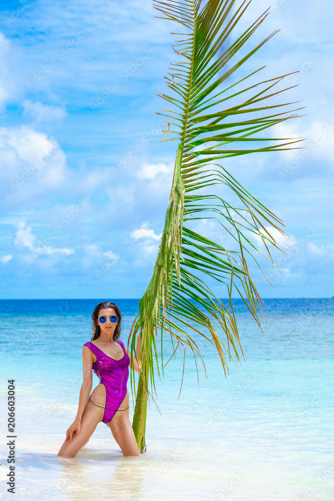 Girl swimsuit with palm branch on background of ocean