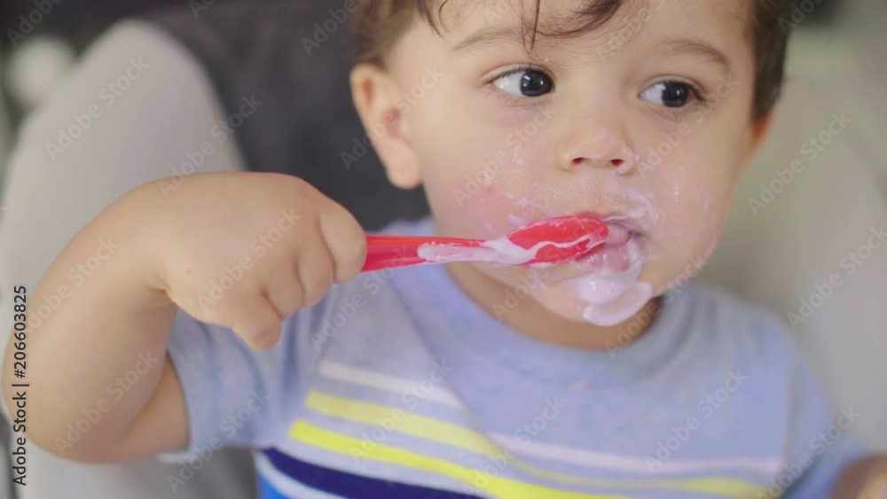 Toddler Eating Yogurt with Spoon Mess. a slow motion close up view of a child eating yogurt with a spoon Toddler Eating Yogurt with Spoon Mess. a slow motion close up view of a child eating yogurt with a spoon