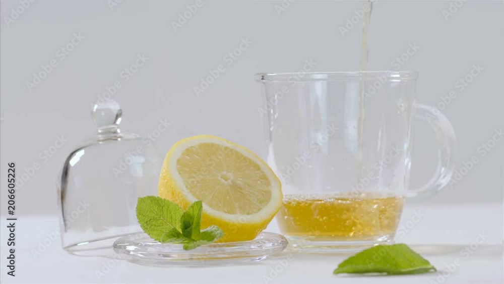 Herbal tea being poured into transparent teapot, lemon and mint leaves around Herbal tea being poured into transparent teapot, lemon and mint leaves around