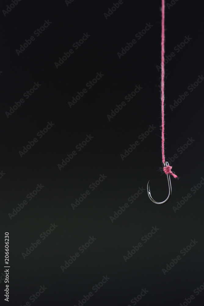 Fishing hook tied with red rope hanging on a black background