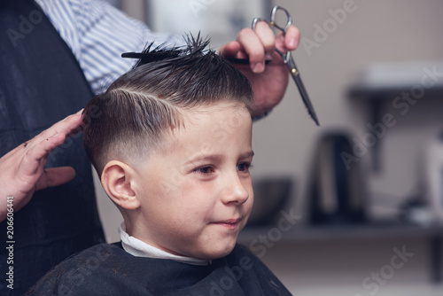 Cheerful Caucasian boy  getting hairstyle in barbershop.