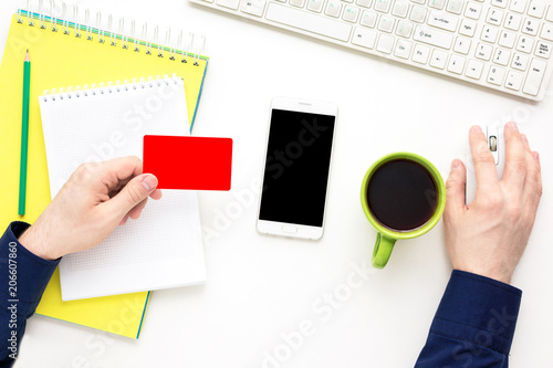 Wallpaper Mural white desk, male hands, guy working at the computer, holds in hand a business card, white smart phone lies on the desk,  office supplies,  white background with copy space, for advertisement, top view Torontodigital.ca