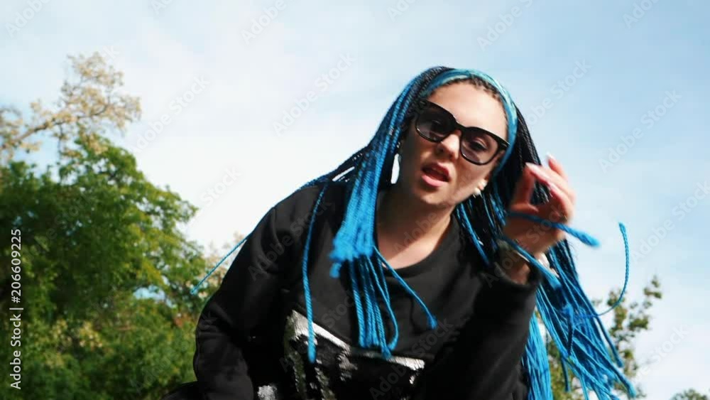 Portrait of cool young woman with african kanekalon blue braids on sky background. Afro hairstyle, freaky dyed hair. Happy hipster girl in black having fun, spinning head. Portrait of cool young woman with african kanekalon blue braids on sky background. Afro hairstyle, freaky dyed hair. Happy hipster girl in black having fun, spinning head.