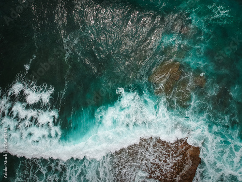 Aerial view of ocean waves and brown rocks in the coastline