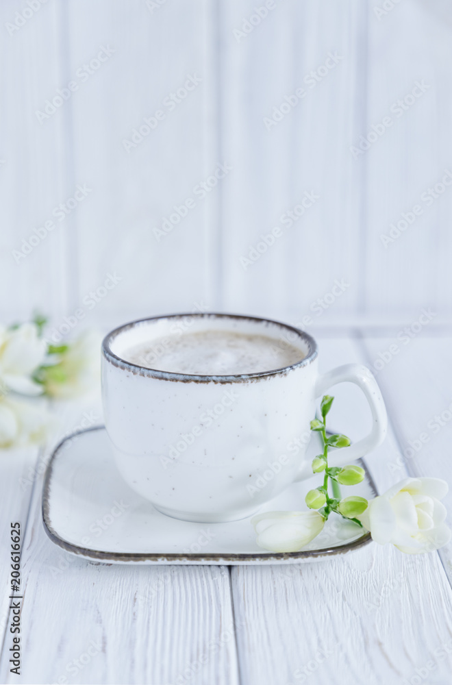 White cup of coffee cappuccino and white freesia flower on white wooden background. Free space, vertical photo White cup of coffee cappuccino and white freesia flower on white wooden background. Free space, vertical photo