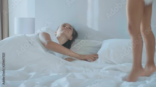 Little girl jumping on bed and wakes up her young mother in the early morning