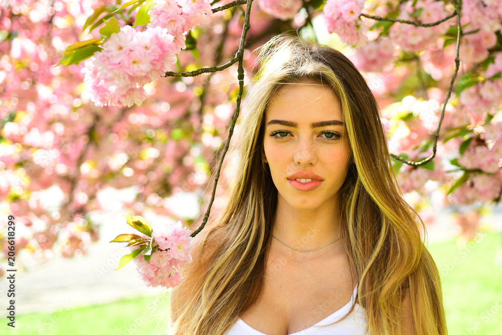 Woman with long blond hair standing under cherry blossom tree. Sensual female radiating confidence over natural background. Girl with tanned skin, full lips and sexy appearance enjoying sunny day Woman with long blond hair standing under cherry blossom tree. Sensual female radiating confidence over natural background. Girl with tanned skin, full lips and sexy appearance enjoying sunny day