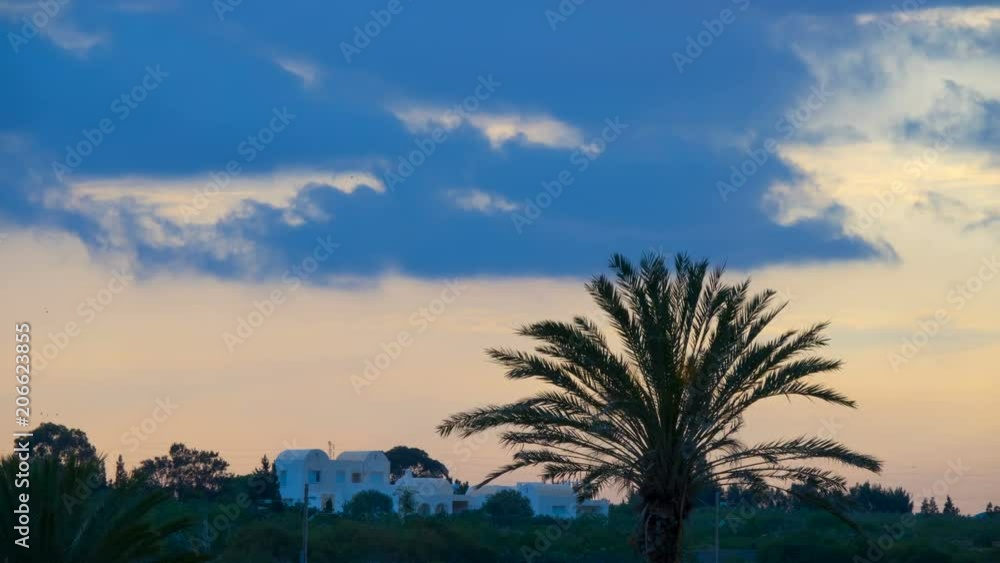 Sunset over white houses and palms . Silhouette of a palm tree over the sunset. Time Lapse. Timelapse. Sunset over white houses and palms . Silhouette of a palm tree over the sunset. Time Lapse. Timelapse.