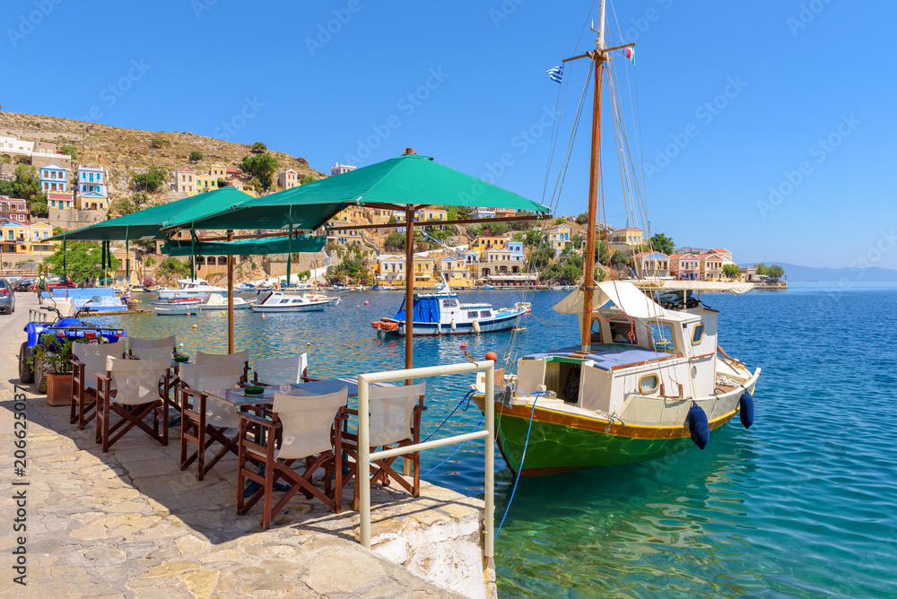 SYMI, GREECE - May 15, 2018: Tables in local traditional restaurant with view of bay and boats. Symi island, Greece