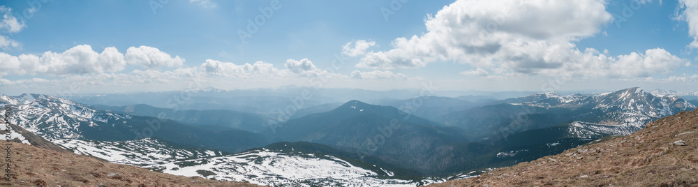 A beautiful panoramic view of the snow-capped mountains of the Carpathians from the top of Goverly in spring in a beautiful sunny day with light clouds. Carpathians, Goverla, Ukraine.