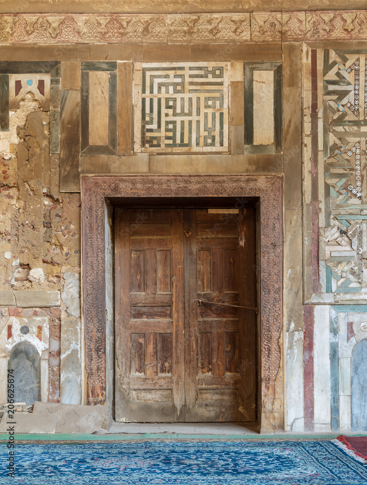 Grunge wooden decorated door on external old decorated marble wall, El Mardani Mosque, Cairo, Egypt Grunge wooden decorated door on external old decorated marble wall, El Mardani Mosque, Cairo, Egypt