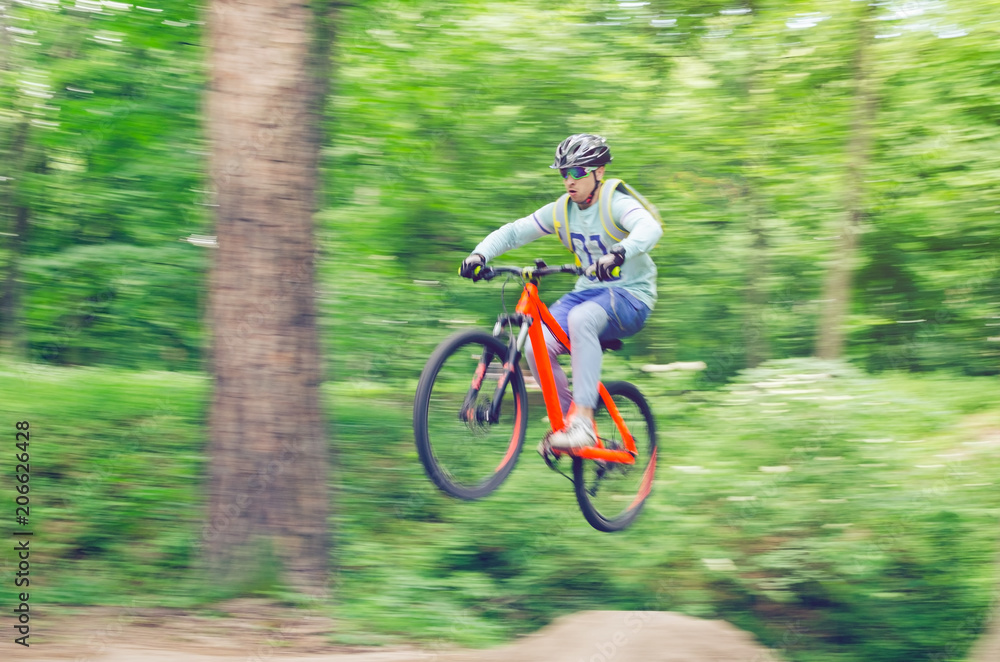 Cyclist in helmet on an orange bike doing a trick in a springboard jump in the forest, motion blur