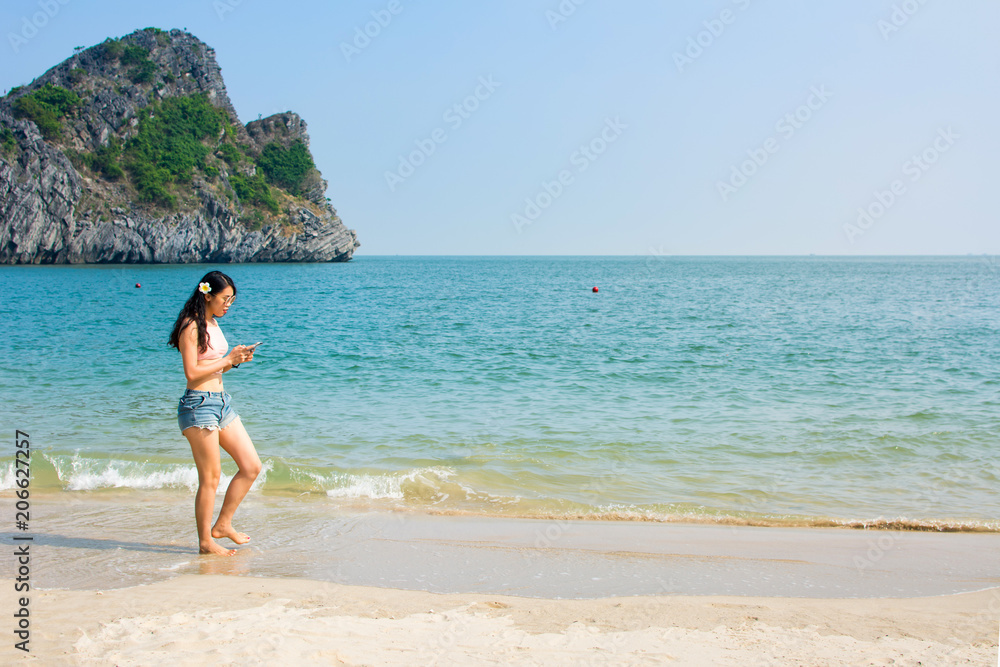 Girl looking at the phone while walking on the beach
