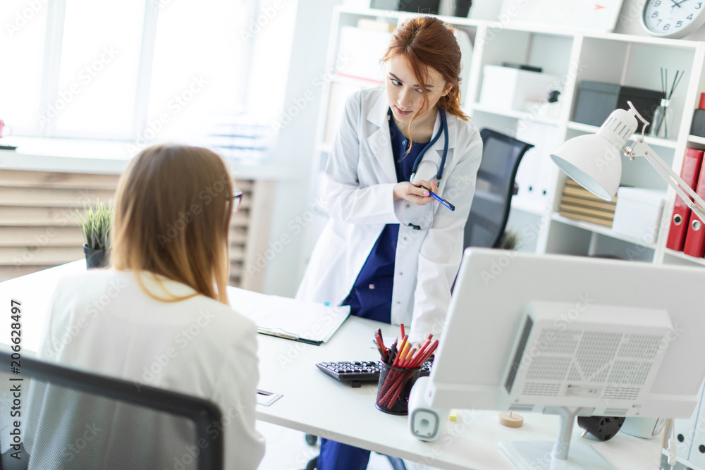 A beautiful young girl in a white robe is standing near a computer desk in the office and communicating with the interlocutor. The girl makes notes in the document. A beautiful young girl in a white robe is standing near a computer desk in the office and communicating with the interlocutor. The girl makes notes in the document.