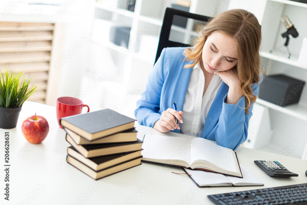 Beautiful young girl sitting at desk in office, holding a pen in her hand and reading a book. Beautiful young girl sitting at desk in office, holding a pen in her hand and reading a book.