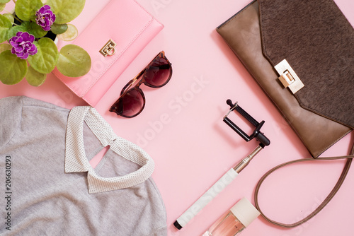 set clothes, a purse and a bag, a comb and sunglasses, a self-stick and eau de toilette. Flowers are next to a pink background. Fashion trends of summer for the women. photo