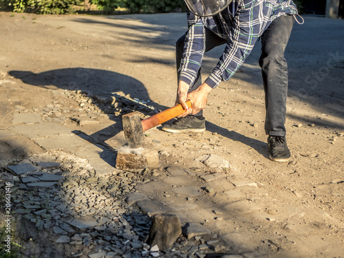 close up person outdoors crushing stone with hand hammer on the dirty ground with dust