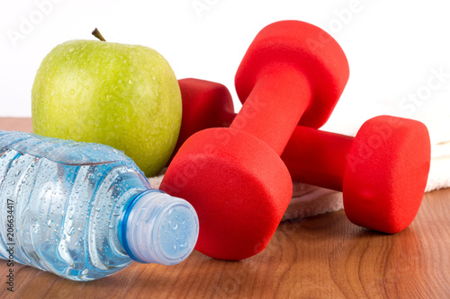 Fresh bottle of water with dew, green apple and red dumbbell on wooden floor. Health food and diet and sport concept. Close up, selective focus