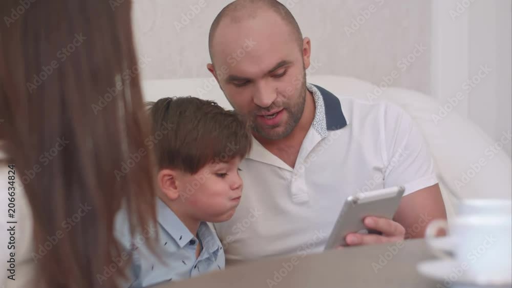 Young father showing something on the tablet to his wife and sons Young father showing something on the tablet to his wife and sons