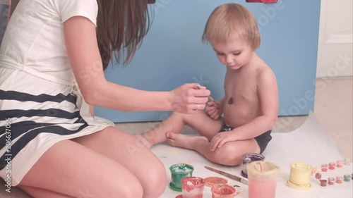 Mother painting on her little boy body making him ticklish