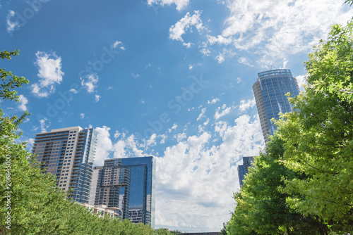 Green public city park in downtown Dallas sunny day. Green tree lush canopy with modern buildings in background cloud blue sky. Urban recreation and outdoor activities concept. photo