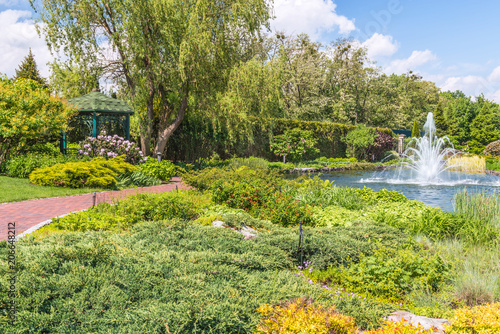 Fragment of the park in Mezhigiri near Kiev. A small fountain on the lake. The flowering bush of the rhododendron  a fragment of the lake and a beautiful gazebo.