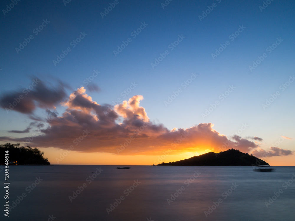 Stunning Beautiful Orange Sunset Long Exposure Landscape over Smooth Flat Sea Ocean and Island with Palm Trees