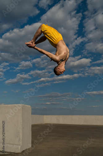 Tricking on street. Martial arts and elements of parkour. Man flips back barefoot. Taken from low angle against sky. photo