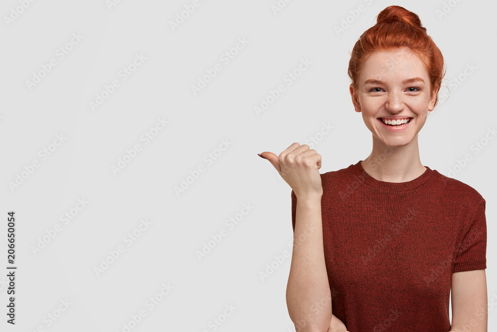 Horizontal portrait of pretty female has shining smile and ginger hair, indicates right at blank copy space for your advertisement or promotional text, being delighted to notices luxury restaurant Horizontal portrait of pretty female has shining smile and ginger hair, indicates right at blank copy space for your advertisement or promotional text, being delighted to notices luxury restaurant