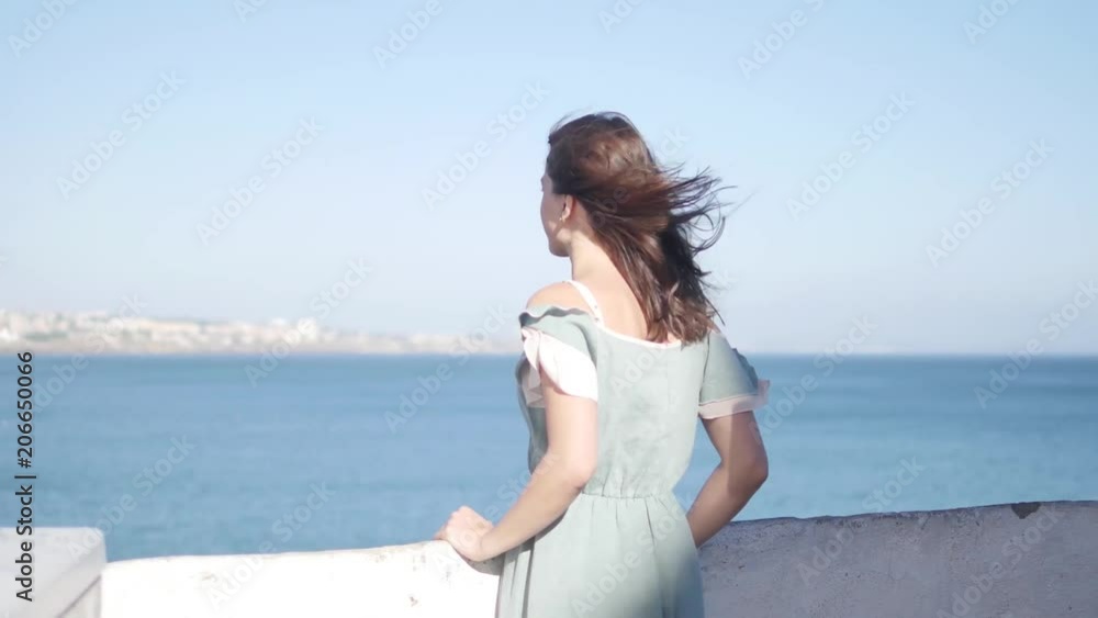 Beautiful brunette Girl relaxing on rock above island and city. Outdoors. Happy Young Woman Enjoying Nature and having Fun over sea and blue sky. Beautiful brunette Girl relaxing on rock above island and city. Outdoors. Happy Young Woman Enjoying Nature and having Fun over sea and blue sky.