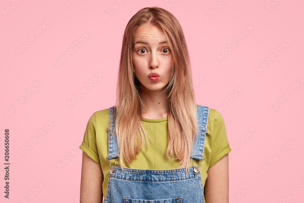 Φωτογραφία Horizontal portrait of pleasant looking female keeps lips round, has long hair, expresses bewilderment as recieves proposal from friend to date, isolated over pink background
