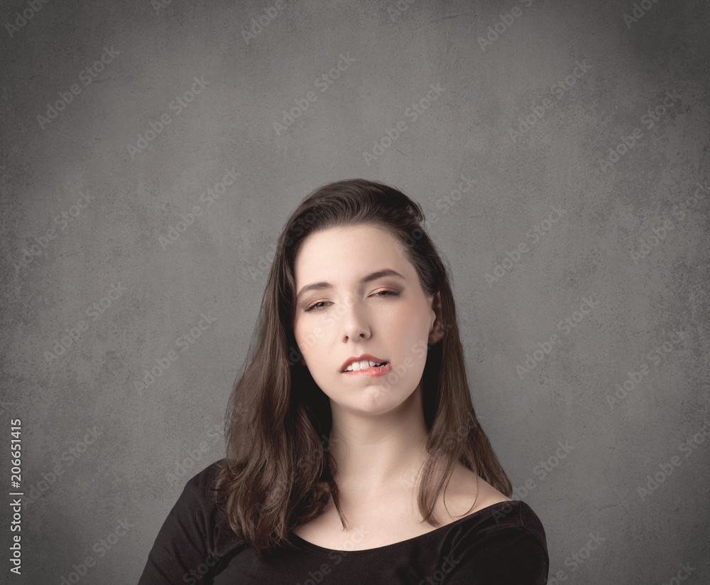 A pretty young teenage girl standing in front of a grey clear empty urban wall background concept while making funny faces. A pretty young teenage girl standing in front of a grey clear empty urban wall background concept while making funny faces.