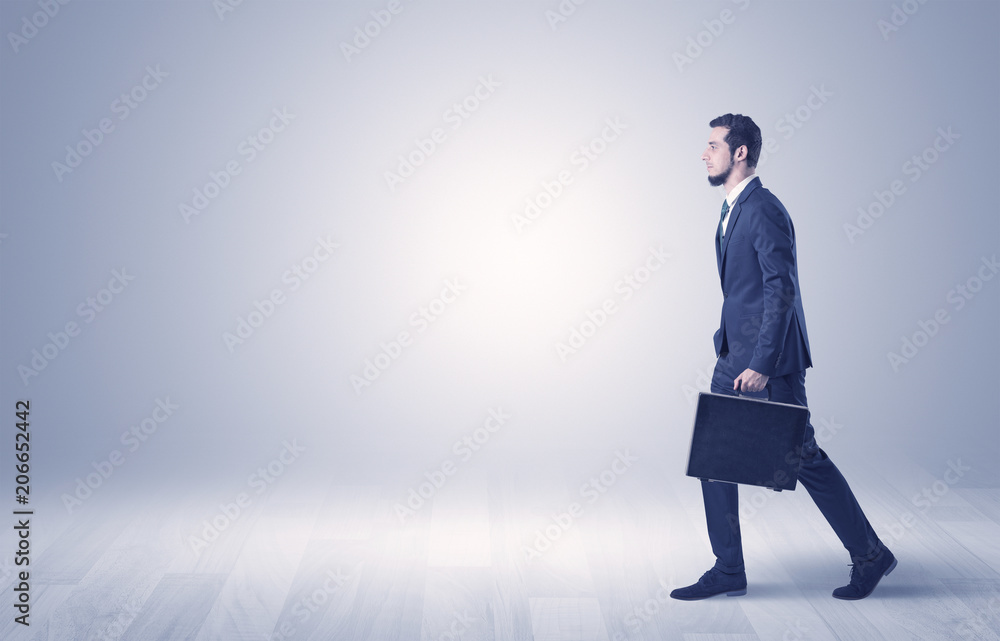 Successful businessman walking in front of an empty wall with briefcase on his hand
Successful businessman walking in front of an empty wall with briefcase on his hand